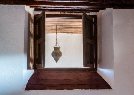 Wooden shutters closing window in thick stone wall of house with small ornate lamp hanging from beams outsideの写真素材