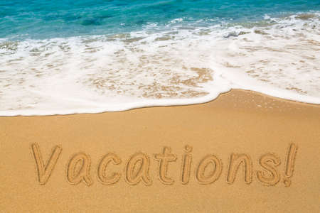 Vacations words written into sand on beach by warm blue ocean in Caribbean advertizing vacations and holidaysの写真素材