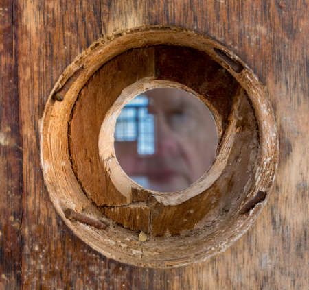Ghostly face looking through a wooden door with small peep hole or viewing lens in the doorwayの写真素材