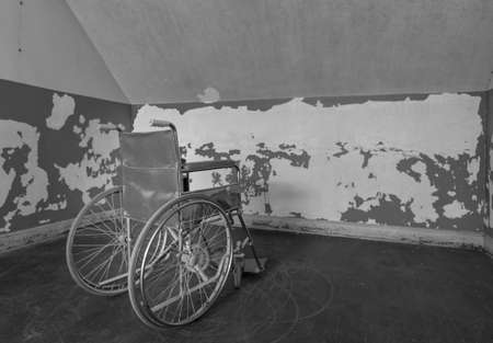 Old wheelchair facing the wall and trapped in corner of a roomの写真素材