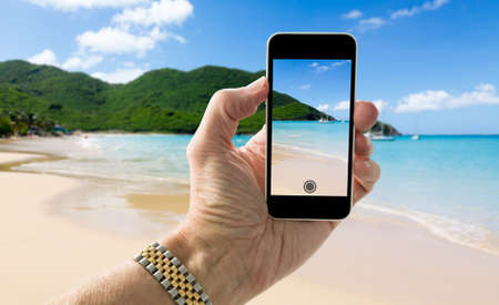 Tourist taking photo on smartphone of Anse Marcel beach on St Martin Sint Maarten Caribbeanの写真素材
