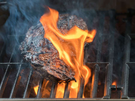 Close up of large piece of steak or beef flaming on barbeque
