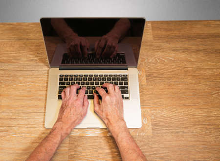Senior caucasian adult man types on modern keyboard of laptop or ultrabook on wooden desk with copy...