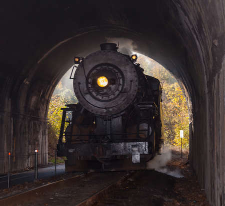 Old steam train pulling into a tunnel belching steam and smoke