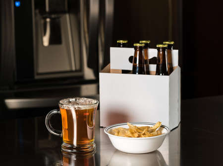 Six pack of brown beer bottles in plain white cardboard carrier on stainless steel kitchen or bar...