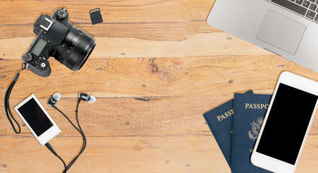 Clean and tidy wooden desk with equipment ready for travel including camera, laptop, phone, music player and passportsの写真素材