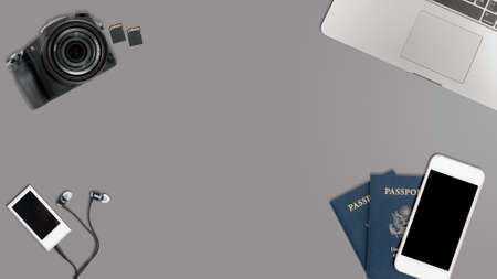 Clean and tidy grey desk with equipment ready for travel including camera, laptop, phone, music player and passportsの写真素材