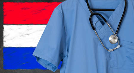 Blue doctor scrubs shirt and stethoscope hang empty in front of Luxembourg flag. Illustration of medical staff coming from other countries to staff health systemsの写真素材