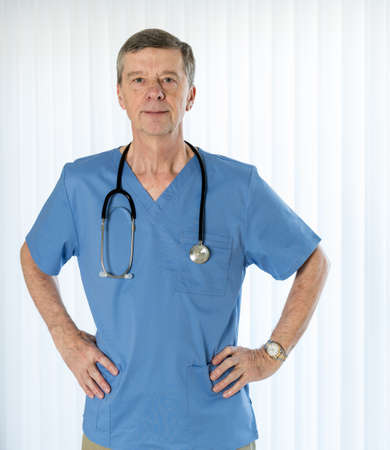 Senior male caucasian doctor with stethoscope in medical scrubs and confidently facing the camera in portraitの写真素材