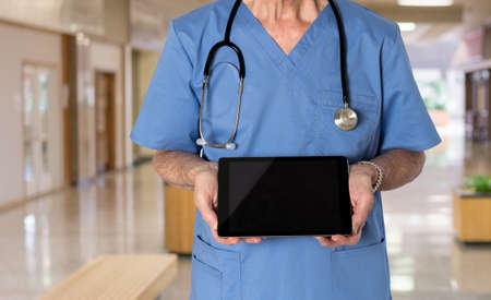 Senior male caucasian doctor with stethoscope in medical scrubs looking up and holding electronic...