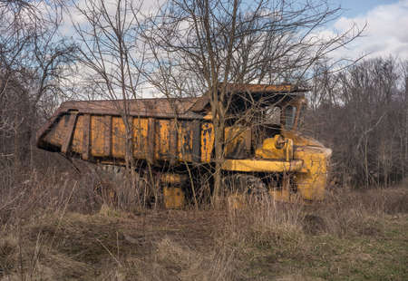 Rusting and overgrown heavy yellow industrial truck and equipment abandoned in economic recession
