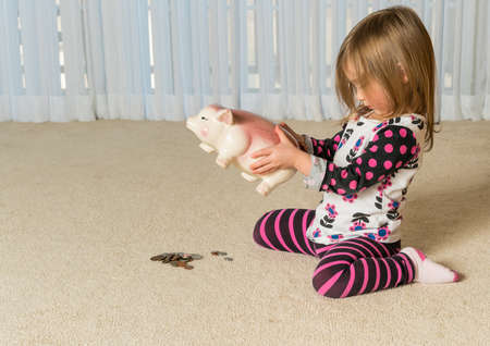 Young girl on floor of home trying to get money to pay off debt  out of a piggy bank for expenses in the futureの写真素材