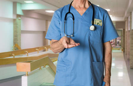 Senior caucasian doctor in scrubs in hospital asking for payment for healthcare in USAの写真素材