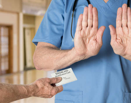 Senior caucasian doctor in scrubs in hospital refusing to treat a patient with a Medicaid card
