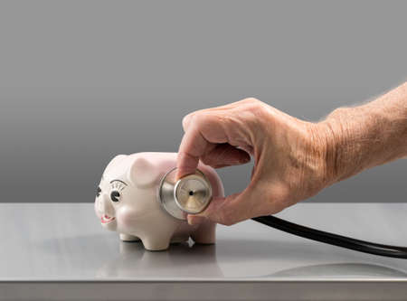 Senior male doctor or vet checking the condition of a small pink piggy bank to illustrate savings or retirementの写真素材