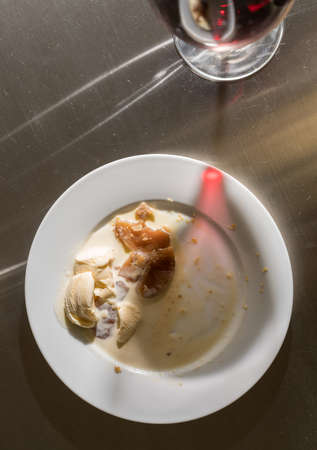 Red wine in large goblet casts a shadow over the remains of a dessert plate and meal on stainless steel counter or tableの写真素材