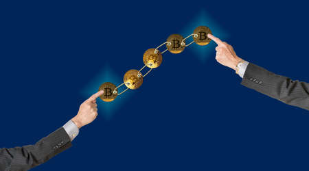Set of gold bitcoins linked by chain on blue background with two arms pointing to ends to illustrate concept of blockchain for supply chain managementの写真素材