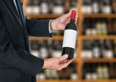 Senior caucasian wine steward offering a bottle of red wine with blank label to a customer in a wine...