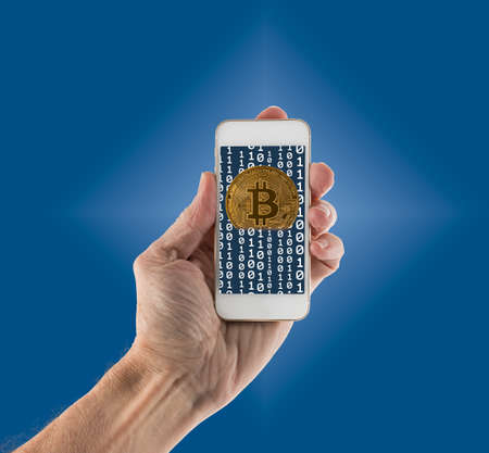 Gold bitcoins on blue background and emerging from app on smartphone to illustrate concept of...