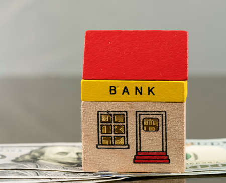 Toy brick bank building sitting on US 100 dollar bills with bitcoin coins inside the windows of the bank suggesting the future is in cybercurrencyの写真素材