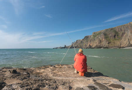 Man fishing in the ocean at Hartland Quay in North Devon, Englandの写真素材