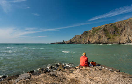 Man fishing in the ocean at Hartland Quay in North Devon, Englandの写真素材