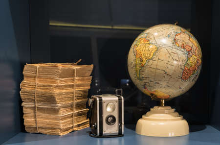 Stack of old worn books and papers with box camera and ancient globe on bookshelfの写真素材