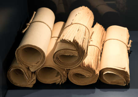 Rolls of old yellowed and worn books and papers tied with string on bookshelfの写真素材