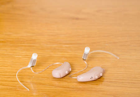 Macro close up of a matched pair of tiny modern hearing aid on wooden bedside dressing table