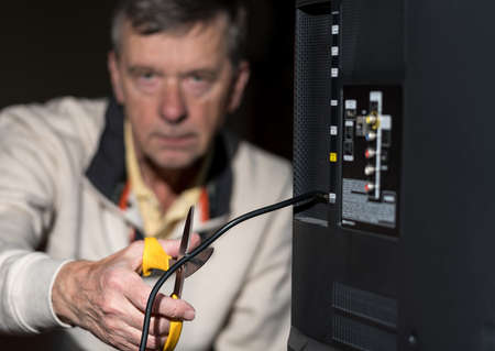Close up of senior caucasian retired man cutting the aerial connection to his TV to illustrate...