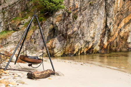 Burned log in large rusty fire pit or barbeque on beach by rocky Norwegian fjordの写真素材