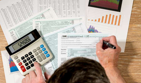 Senior man completing USA tax form 1040 for 2017 with charts and calculations on wooden deskの写真素材