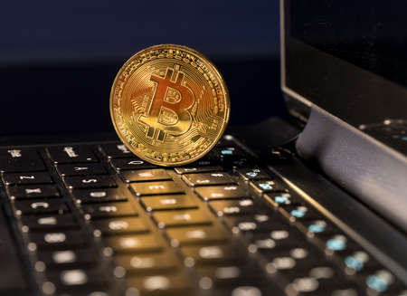 Single bitcoin coin standing on the keyboard of modern laptop computer