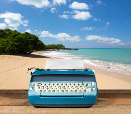 Modern electric typewriter on wooden desk with ocean beach background suggesting deserted islandの写真素材