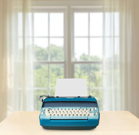 Concept image of working from home with electric typewriter on desk in front of bright summer window onto gardenの写真素材
