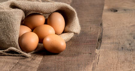 Easter background with brown organic eggs arranged inside a burlap sack on rustic wooden tableの写真素材
