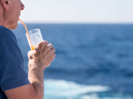 Senior caucasian adult man with tequila sunrise in glass on teak balcony rail of ocean cruise shipの写真素材