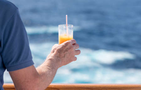 Senior caucasian adult man with tequila sunrise in glass on teak balcony rail of ocean cruise shipの写真素材