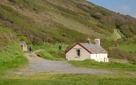 Hikers near a stone cottage on coastline near Hartland Quay on North coast of Devon