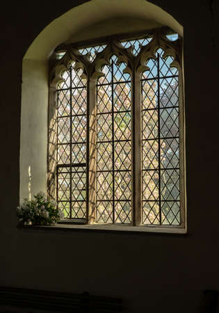View through an old stained glass church window to flowering trees outside in sunshine