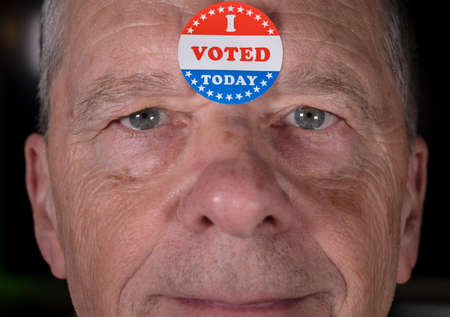 I Voted Today sticker on senior caucasian mans forehead with warm smiling look at cameraの写真素材