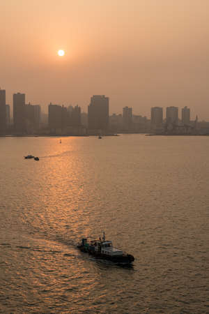 Sun rising in the distance over city skyline of large tower blocks of Qingdao in China