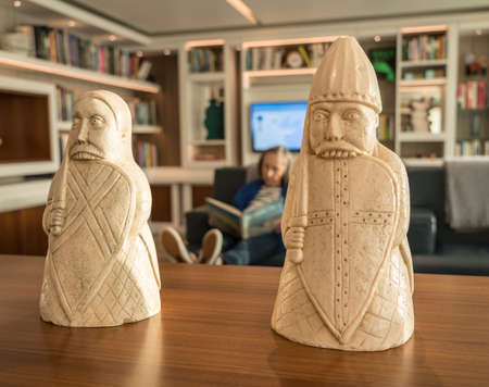 Woman relaxing and reading a book in a study fronted by Lewis Chessmen modelsの写真素材