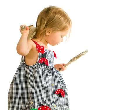 Young smiling caucasian toddler girl brushing blonde hair with silver brush and looking into mirror. Isolated against whiteの写真素材