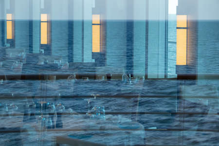Reflections of ocean in windows around modern restaurant on luxury cruise ship at sea
