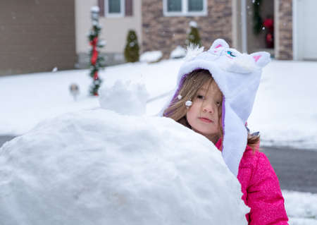 Young toddler girl playing in the snow and making a snowmanの写真素材