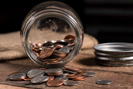 Poverty concept image with a few small coins remaining in a glass savings jar on wooden tableの写真素材