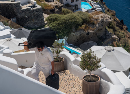 SANTORINI, GREECE - 18 MAY 2019: Hotel porter carries luggage up cliff steps in village of Oia on Santoriniのeditorial素材