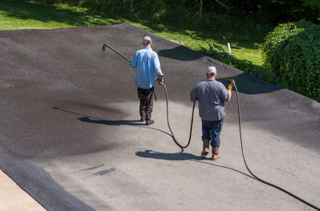 Workers applying blacktop sealer to asphalt street using a spray to provide a protective coat against the elementsの写真素材