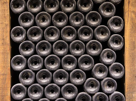 Stacks of wine bottles laying flat in wooden racks in old wine cellar or caveの写真素材
